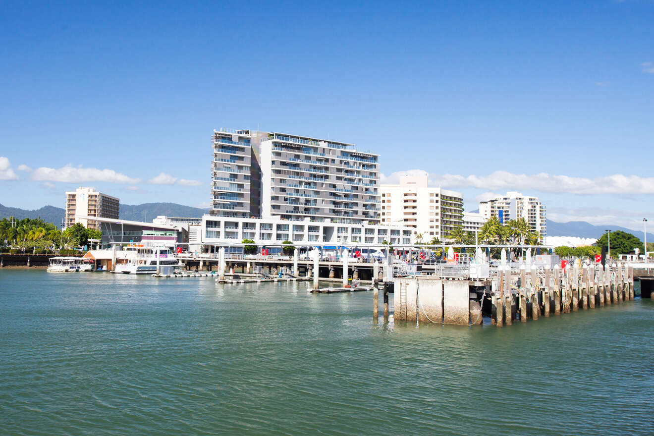 Waterfront at Cairns Esplanade scene with modern buildings and a marina filled with boats under a clear sky, likely in a coastal city